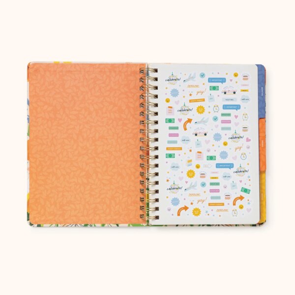 Notebook open showing inside of cover to be orange with lighter orange leaf pattern, showing the first page including stickers